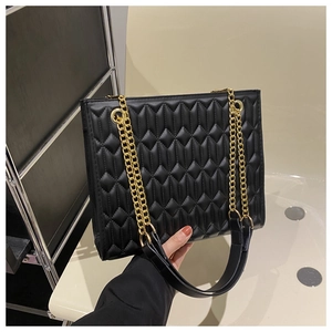 Detail of black quilted leather shoulder bag with gold chain strap and padded handle