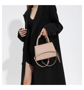 Détail d'un sac à main beige à motif crocodile porté par un mannequin en blazer noir