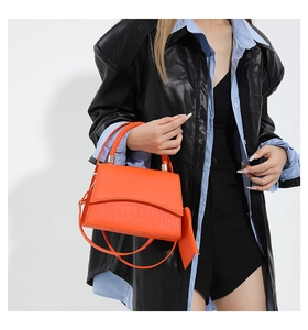 Détail du sac à main orange vif à motif crocodile avec poignée tressée et mini pochette