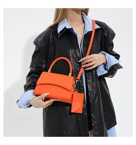 Détail du sac orange à motif crocodile avec poignée tressée et petit porte-cartes assorti
