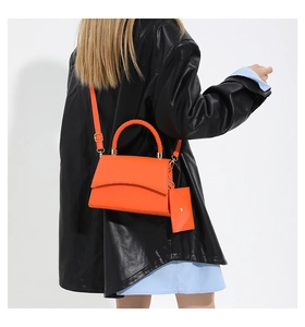 Modèle portant un sac à main orange vif effet crocodile avec petite pochette