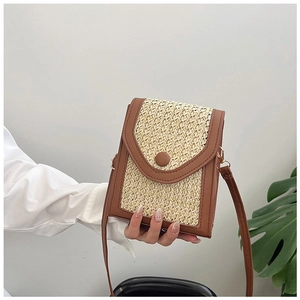 Detail of straw woven crossbody bag with brown leather trim and circular buckle closure