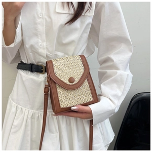 Detail of woven straw crossbody phone bag with brown leather trim on a white dress
