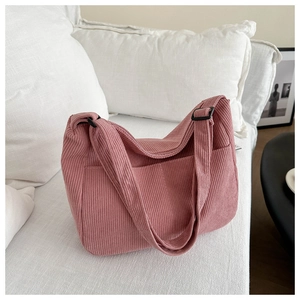 Adjustable black buckle detail on soft pink corduroy shoulder bag over a white sofa