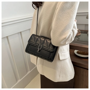 Gros plan d'un sac matelassé noir avec chaîne porté sur un blazer blanc élégant
