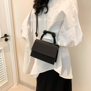 Black woven texture flap bag with artistic knotted top handle worn with white shirt