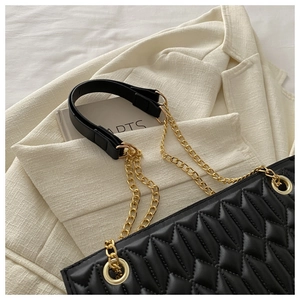 Detail of black quilted leather shoulder bag with gold chain strap on tweed blazer