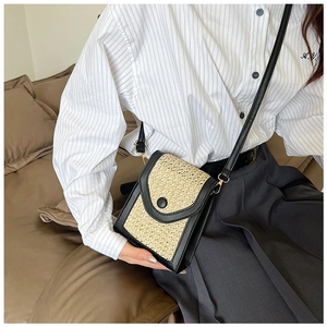 Detail of straw woven crossbody bag with black leather trim worn on a white shirt