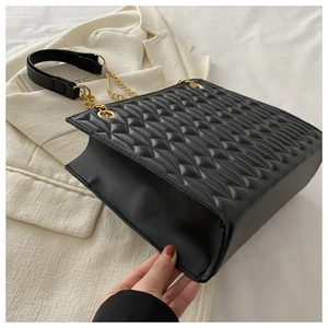 Detail of black quilted tote bag with golden metal chain strap and luxury leather texture