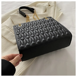 Detail of black quilted PU leather bag with golden chain strap on a white blazer