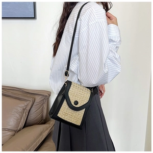 Detail of woven straw crossbody phone bag with black leather trim shown on model