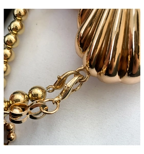Detail of the golden shell-shaped bag featuring glossy metal finish and beaded chain