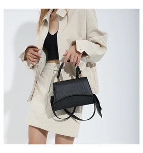 Détail d'un sac à main noir motif crocodile avec poignée tressée et boucles dorées sur mannequin