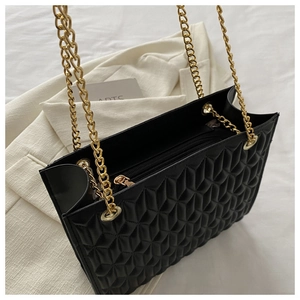 Detail view of black quilted tote bag featuring gold chain straps and zipper closure