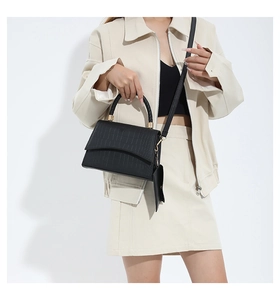 Détail du sac à main noir texture crocodile avec poignée tressée et boucles dorées sur modèle