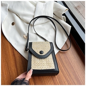 Straw mini crossbody bag with black leather trim on a textured wooden surface