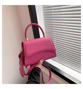 Détail d'un sac à main rose à motif crocodile avec poignée tressée et finitions dorées