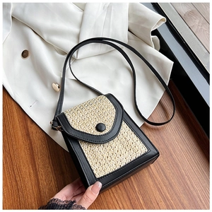 Close-up of small woven straw crossbody bag with black faux leather trim on wood surface