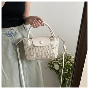 Détail du sac en paille avec broderie florale et finitions en similicuir blanc
