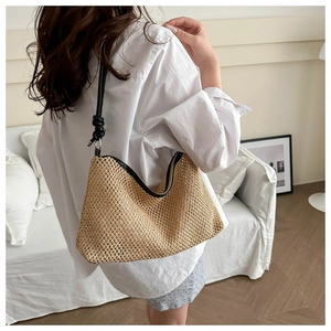 Detail of woven straw hobo bag featuring black leather shoulder strap with knot detail