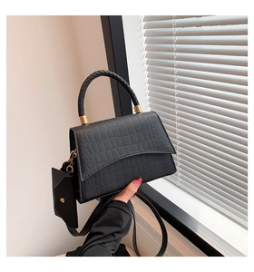 Détail du sac à main noir texture crocodile avec poignée tressée et finitions dorées
