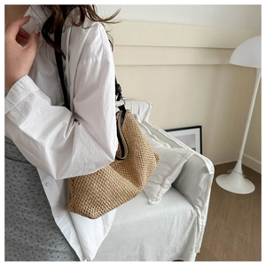 Side view of beige woven hobo bag with black strap worn by a model in a minimalist setting