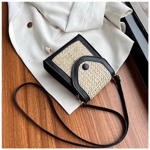 Detail of handwoven straw crossbody bag with black leather flap on a white blazer