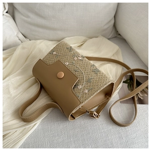 Detail of woven crossbody bag featuring floral embroidery and khaki leather flap closure