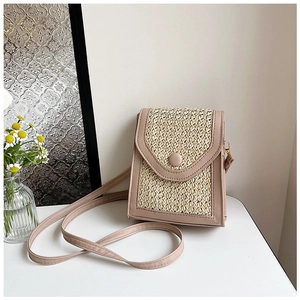 Detail of straw woven panel and pink faux leather trim on a vertical crossbody phone bag