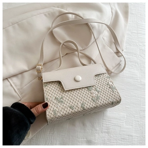Detail of cream woven shoulder bag featuring green floral embroidery and round button clasp
