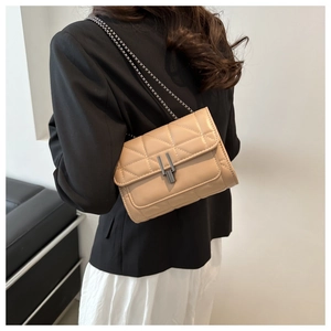 Détail d'un sac bandoulière beige matelassé avec chaîne porté sur un blazer noir
