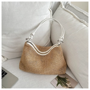 Detail of woven straw tote bag featuring white straps with knot design and metal hardware