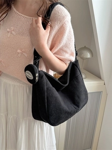 Large black corduroy hobo shoulder bag with a small round pouch in a cozy room setting