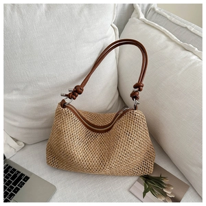 Detail of woven straw tote bag featuring brown leather knotted shoulder strap and silver buckle