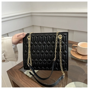 Detail of black quilted faux leather handbag with gold-tone dual chain straps and padding
