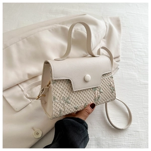 Detail of beige woven handbag with elegant floral embroidery and matte leather handle