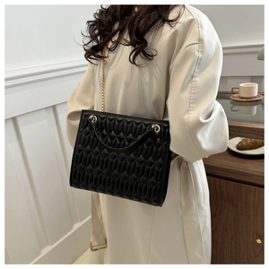 Detail of black quilted leather texture and gold chain strap on a women shoulder bag
