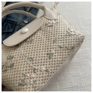 Détail de la texture tissée et broderie florale sur un sac à main en paille avec rabat