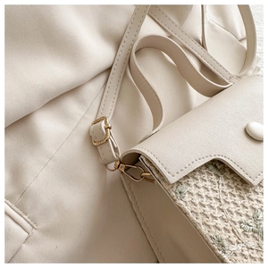 Detailed close-up of cream woven handbag with green floral embroidery and gold hardware