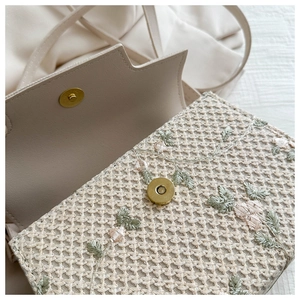 Detailed close-up of floral embroidery on a woven crossbody bag with a magnetic snap button