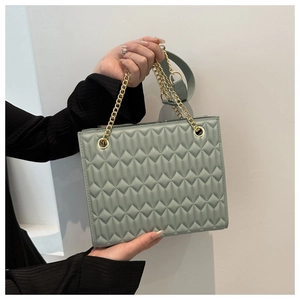 Close-up of light green quilted square bag with gold chain handle and leather strap
