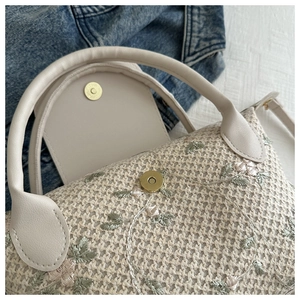 Gros plan détaillé de la broderie florale sur un sac tissé beige avec anse en cuir