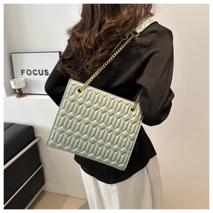 Detail of light green quilted chain shoulder bag with gold metal strap on model