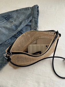 Woven straw tote bag with black leather straps and silver buckles on a white fabric background