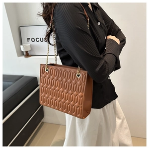 Detail of brown quilted faux leather tote bag with elegant gold chain strap texture