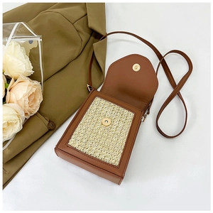 Close-up of woven straw shoulder bag with brown leather trim and golden magnetic clasp