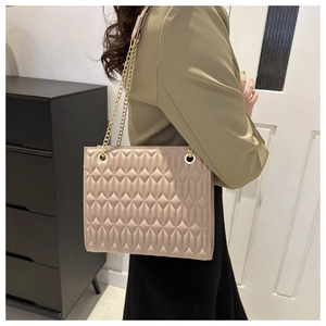 Side view of pink quilted tote bag with gold chain strap on female model in home setting