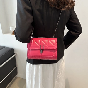 Petit sac bandoulière matelassé fuchsia avec chaîne porté sur un tailleur noir