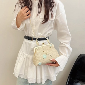 Detail of woven chain bag with light blue floral embroidery and gold metal handle