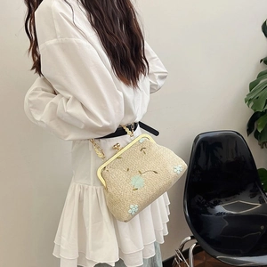 Detail of woven straw crossbody bag with blue floral embroidery and a chain strap